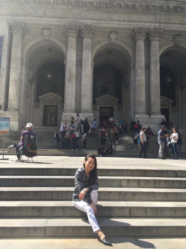 beautiful young asian female international student sitting on the steps in front of New Your city library